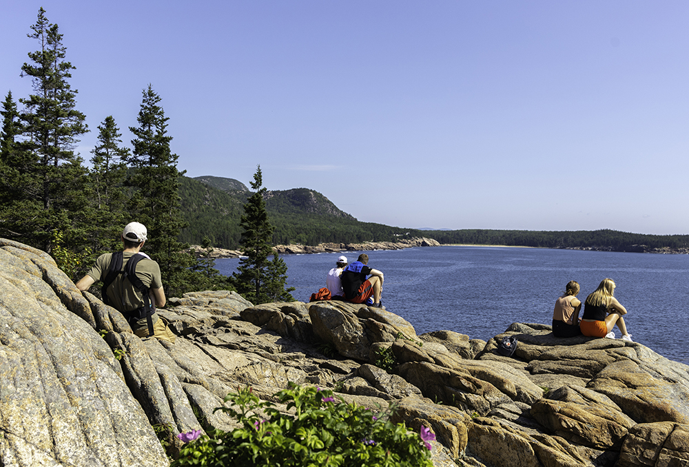 Visitors sit watching the ocean at Otter Cliffs along Park Loop Road in Acadia National Park